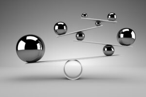 Six metallic spheres of varying sizes are balanced on white flat rods and a circular base, creating a geometric structure against a neutral gray background.